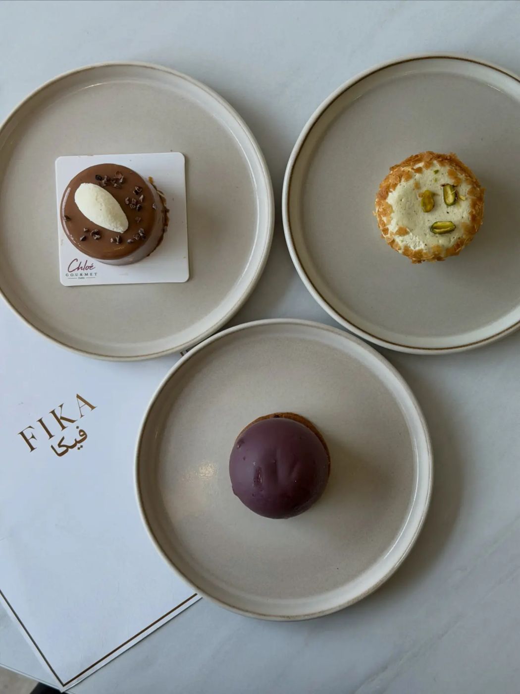 Three patisserie desserts on ceramic plates beside the FIKA menu