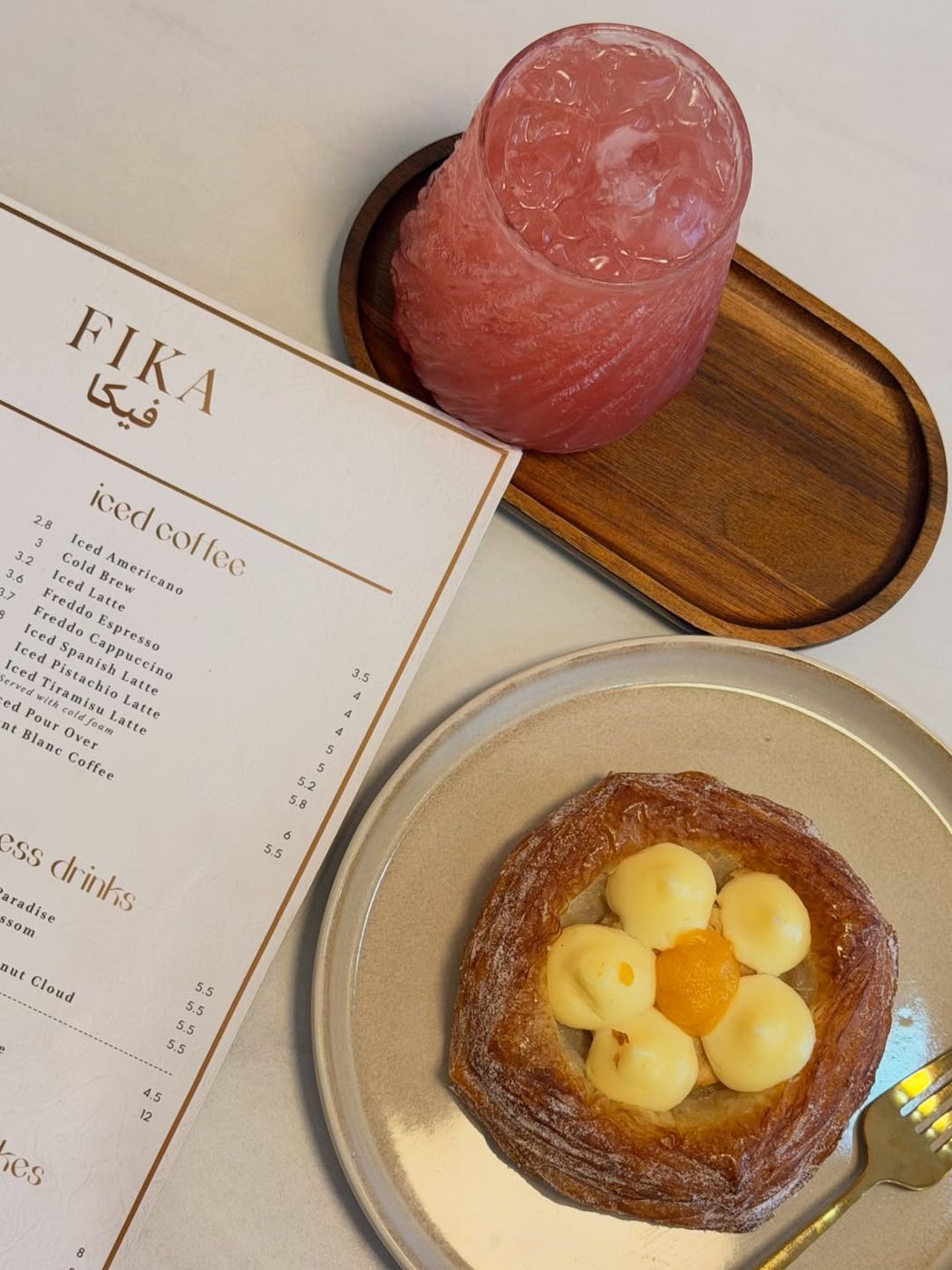 Iced fruit drink and a custard danish next to the FIKA iced coffee menu